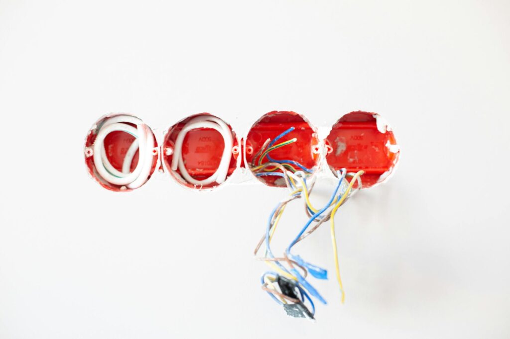 electrician installing three‑hole outlet with red, green, and yellow wires close‑up hand view